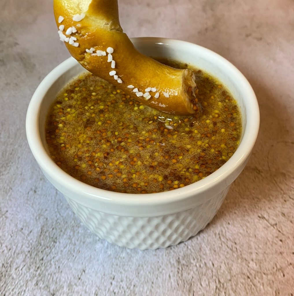 soft pretzel being dipped in sweet mustard dip.