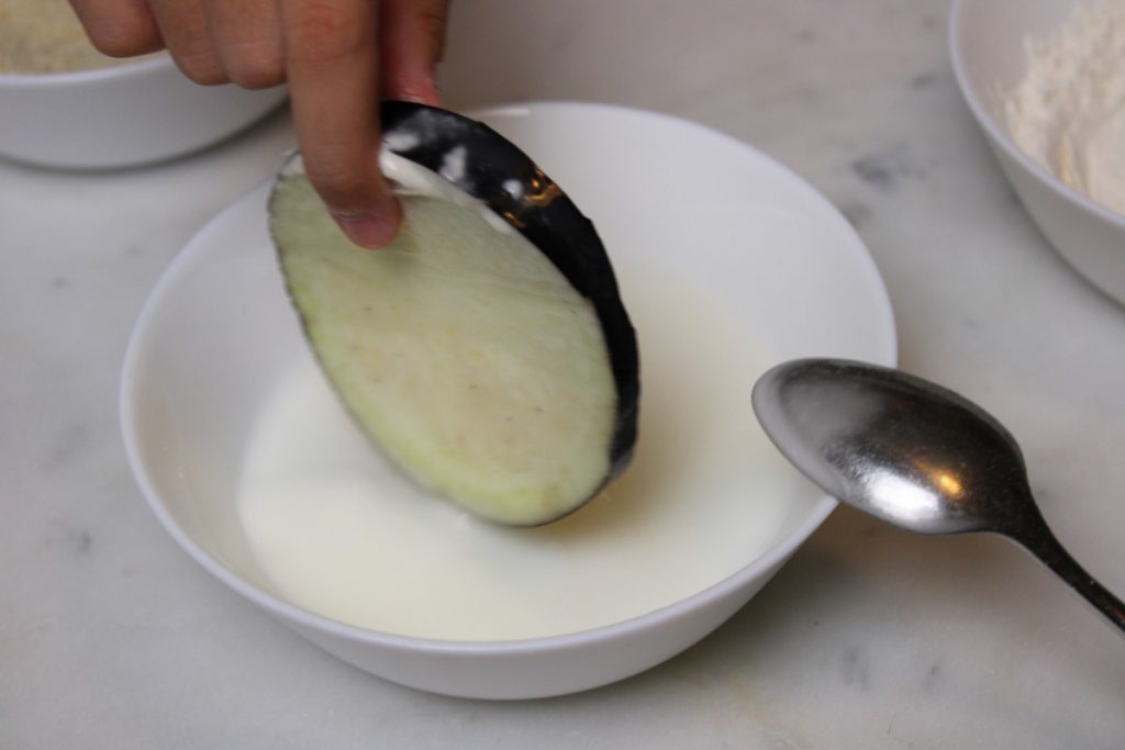 eggplant slice being dipped in cornstarch and water mixture.