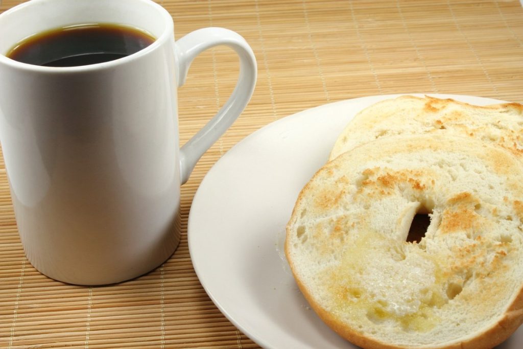 Toasted bagel on a plate with a mug of coffee.