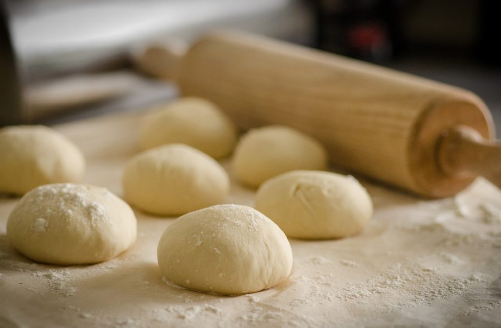 several pizza dough balls with a rolling pin.