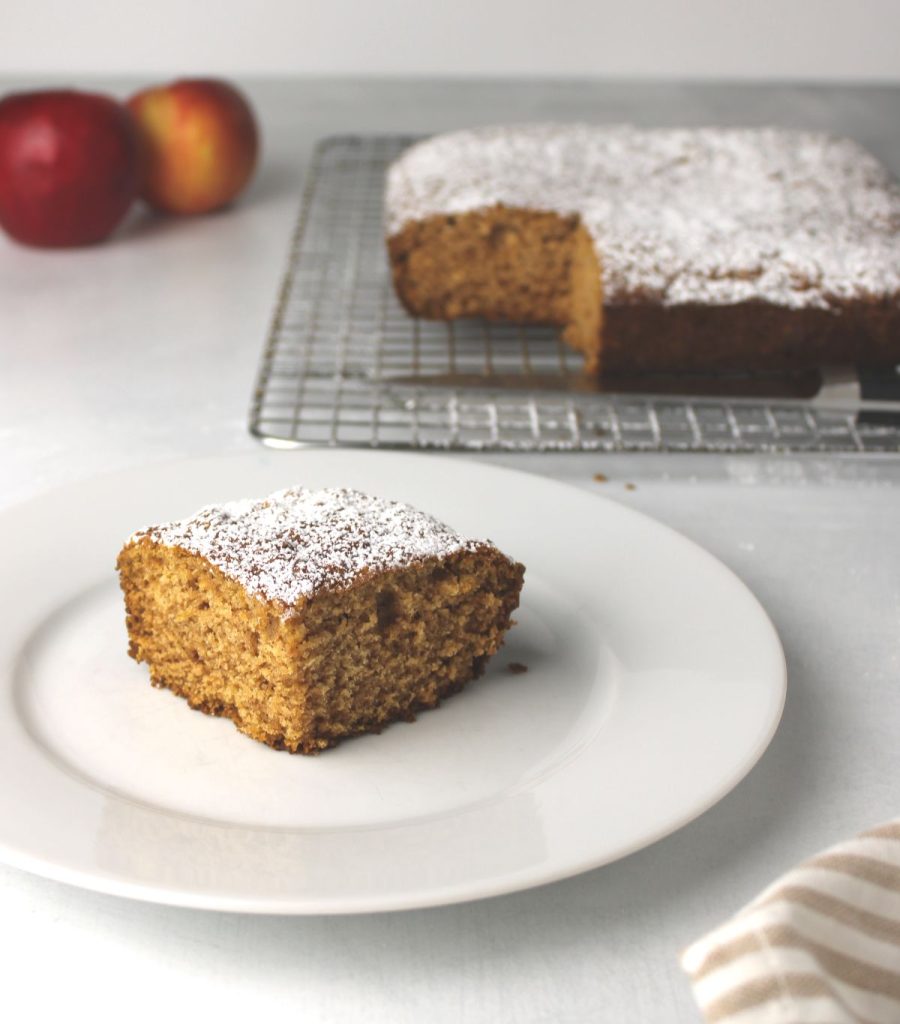 Slice of applesauce cake with cooling cake in the background.