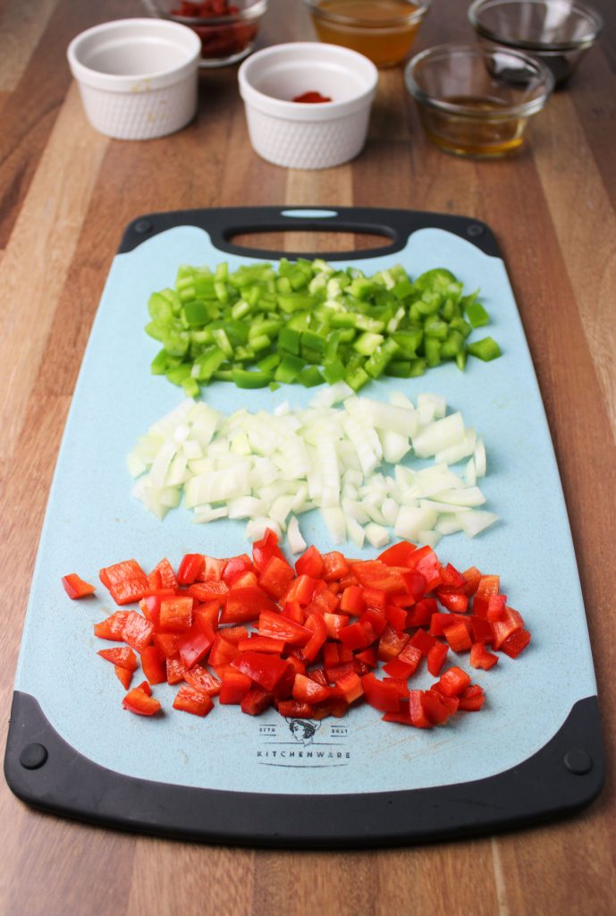 Cutting board with red and green peppers and onion.