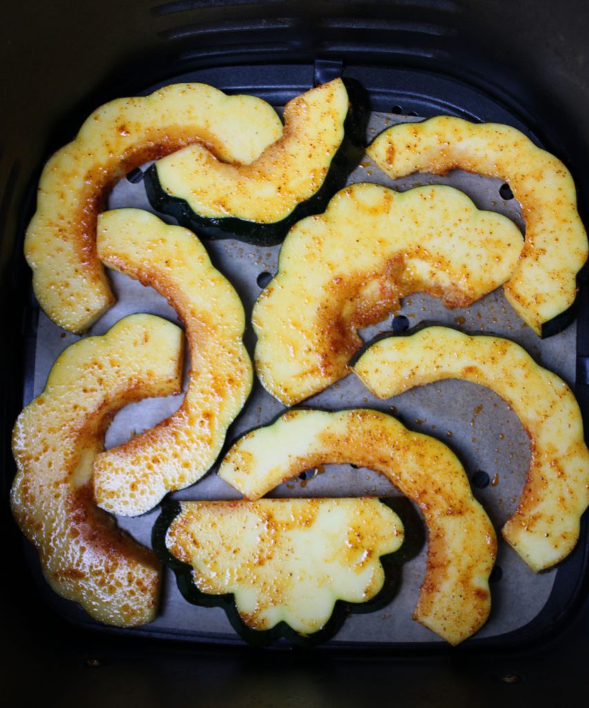 Slices of acorn squash unbaked in the air fryer basket.