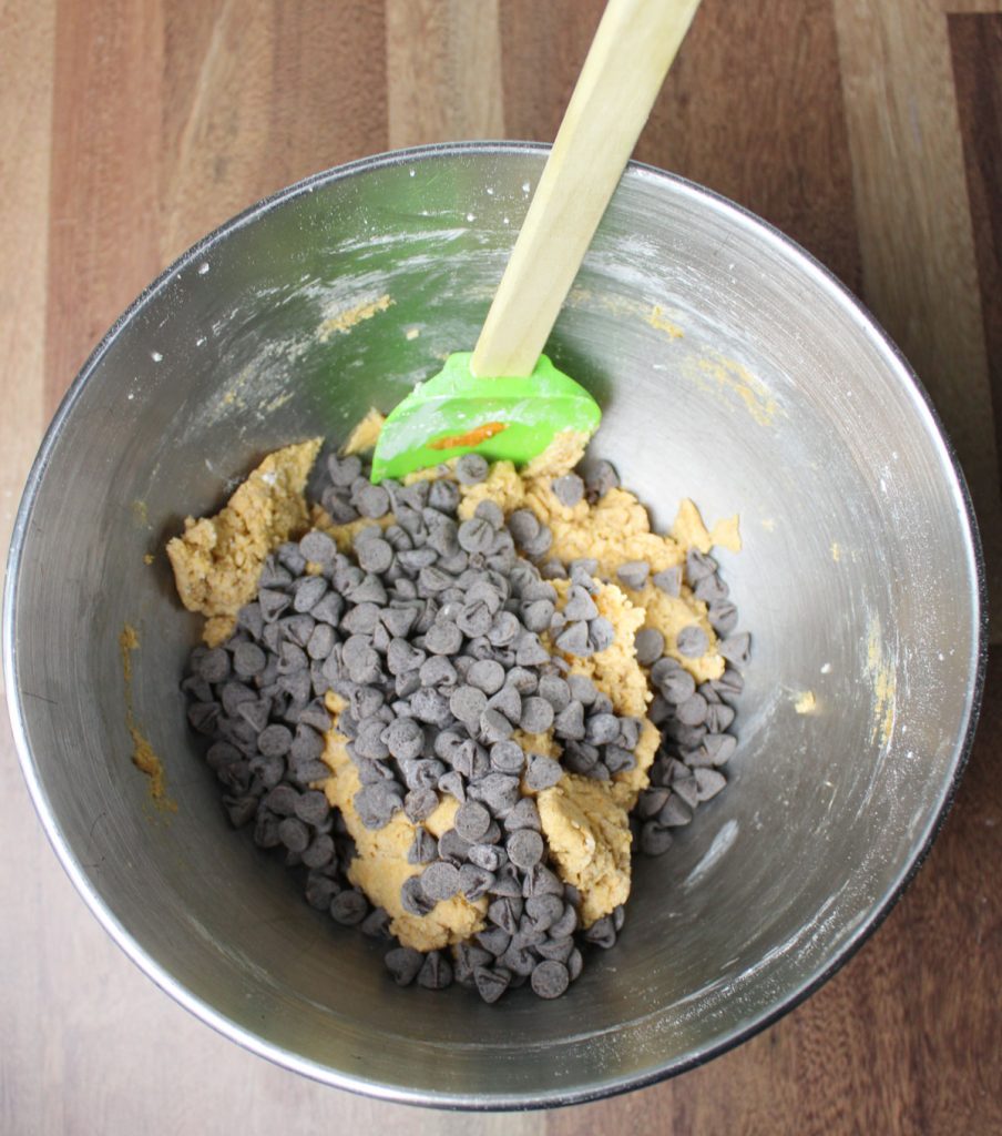 Chocolate chips being mixed into cookie dough.