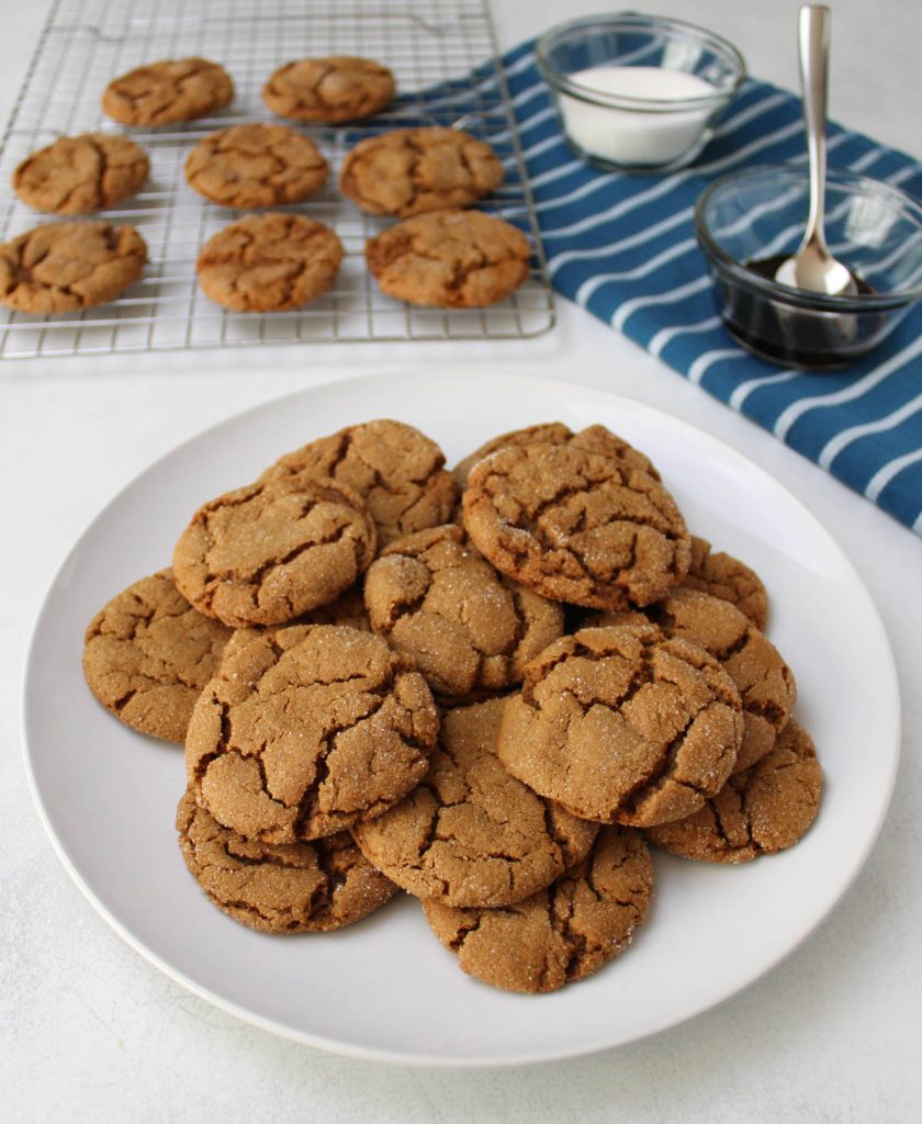 Plate of molasses cookies with cookies cooling in the background.