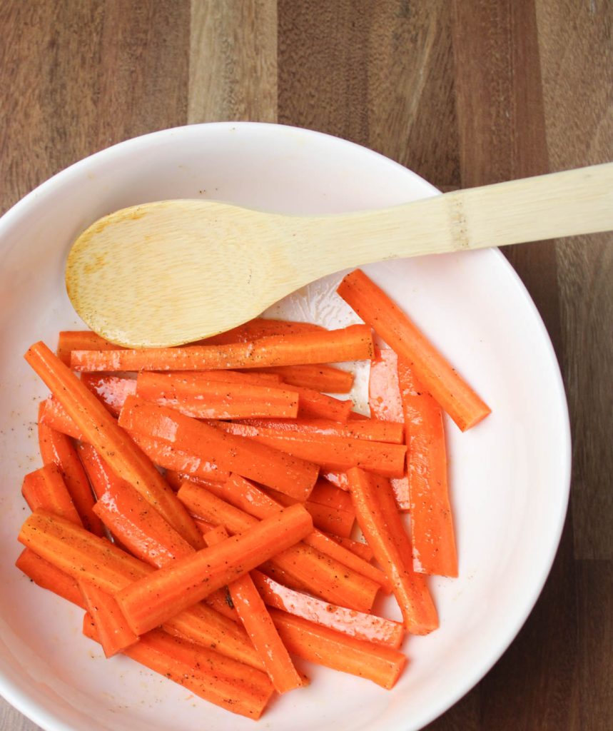Carrot pieces in bowl with olive oil and seasoning.