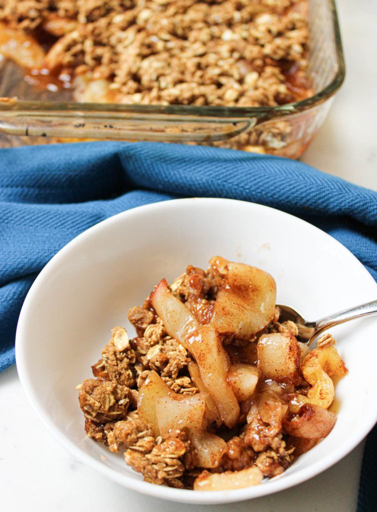 Bowl of apple crisp with baking dish in background.