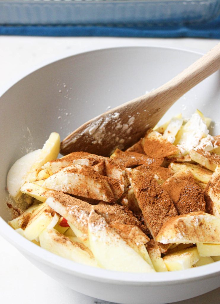 Apple slices in a bowl with cinnamon and flour.