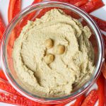 Bowl of hummus with red pepper slices.
