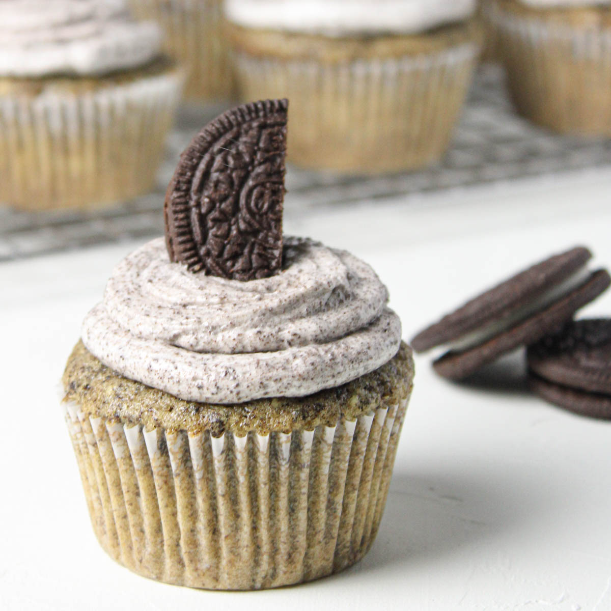 Cupcake with half an Oreo on top with cupcakes in the background.