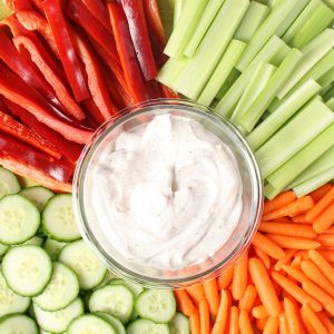 Bowl of dip with celery, red pepper, cucumber and baby carrots.