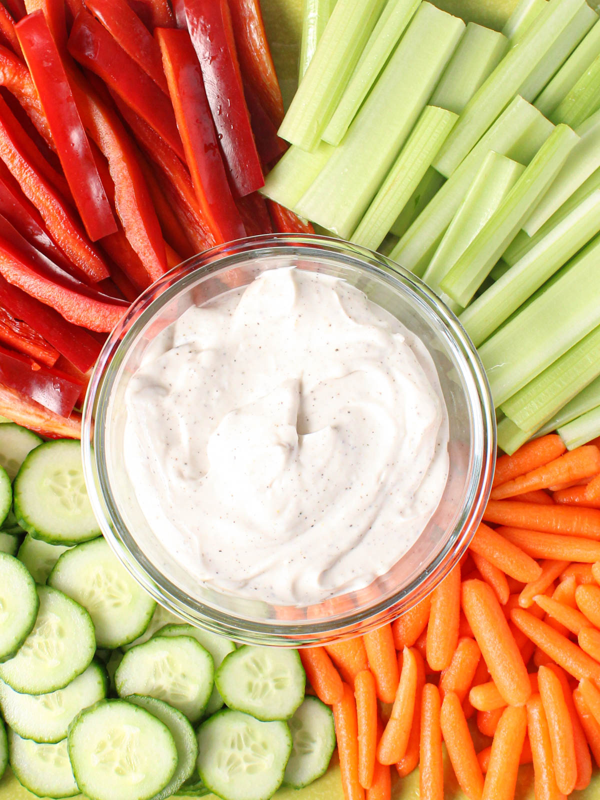Bowl of dip surrounded by celery, carrots, cucumbers and red peppers.