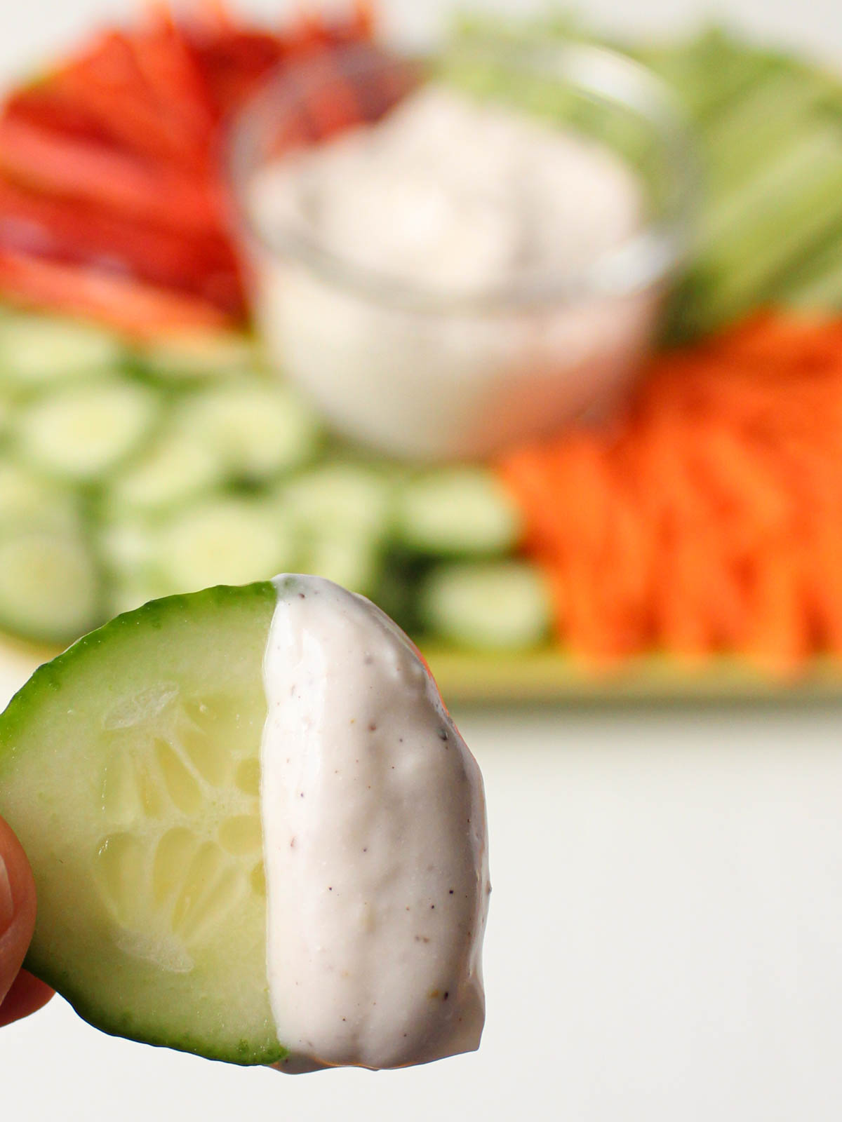 Cucumber slice with dip on it with vegetable platter in the background.